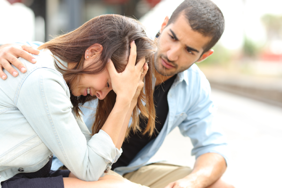A man is comforting a woman who is sitting on the ground.